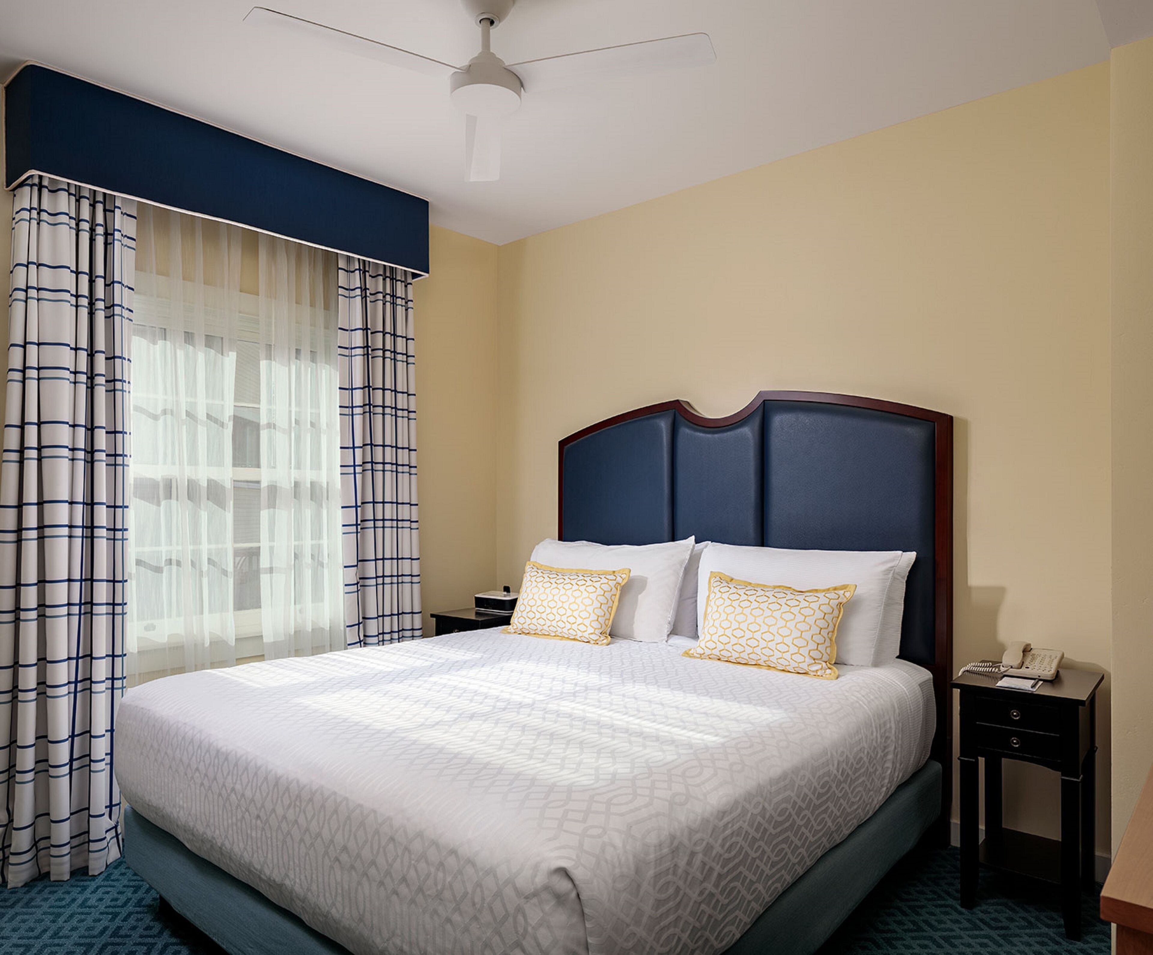 A hotel room with a large bed, a nightstand, a telephone, and a ceiling fan.