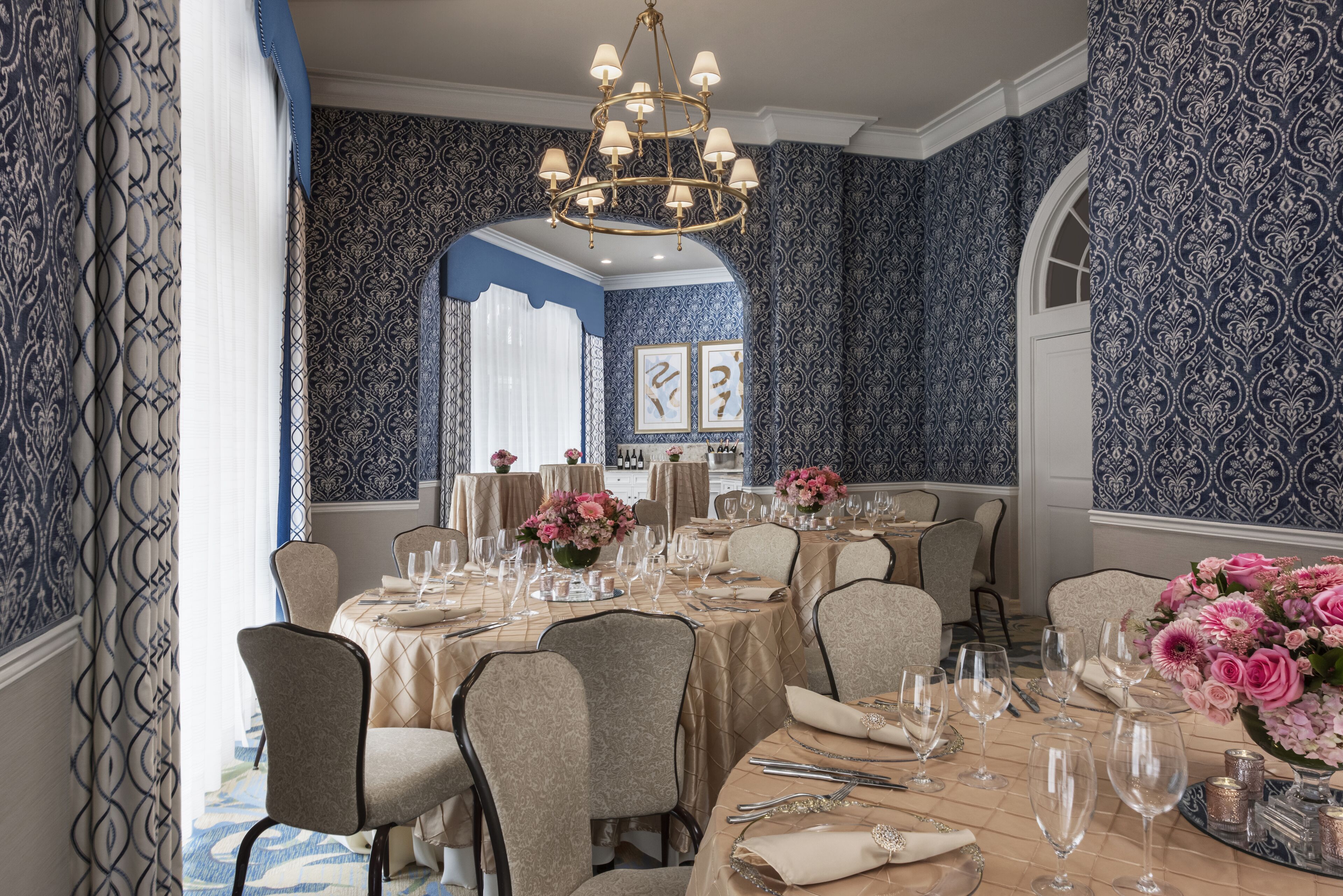 Una sala da pranzo formale con un lampadario, carta da parati decorata e un tavolo apparecchiato per un pasto.