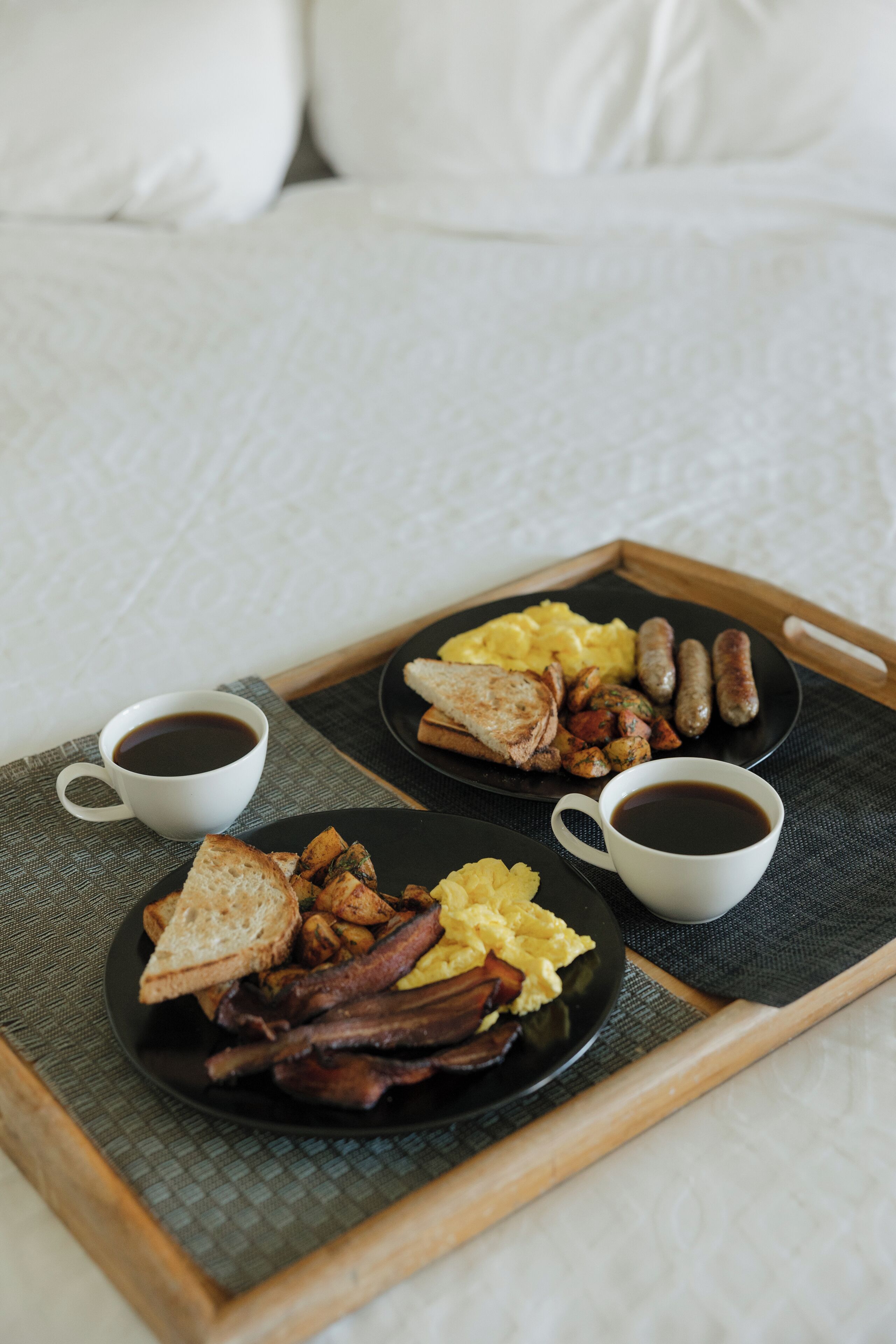 A breakfast tray with toast, eggs, sausages, and bacon on a bed.