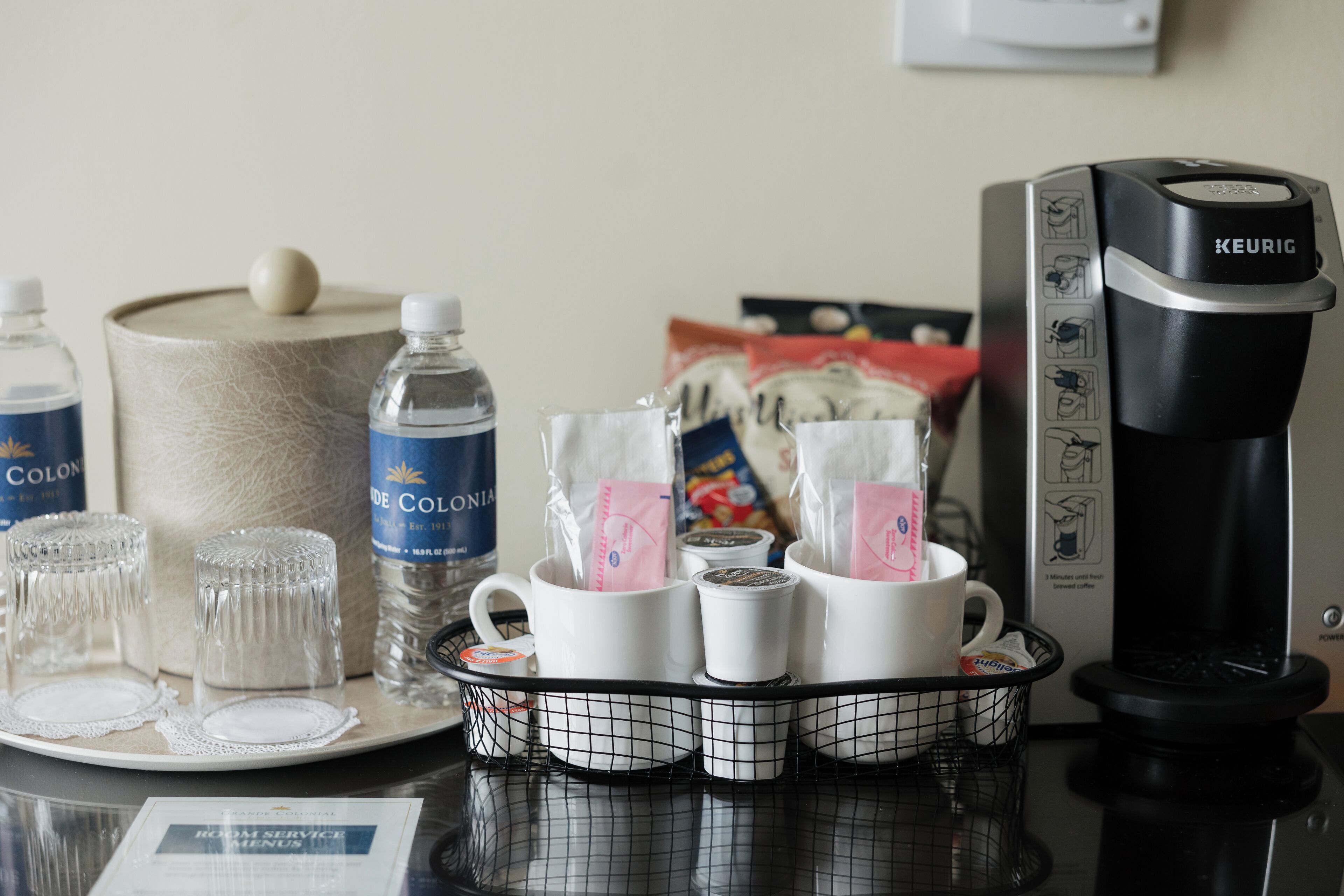 A coffee maker, water bottles, and cups on a table.