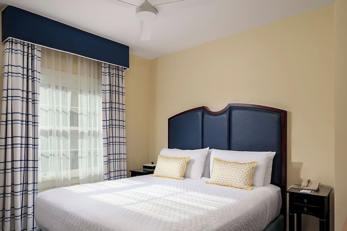 A hotel room with a large bed, a nightstand, a telephone, and a ceiling fan.