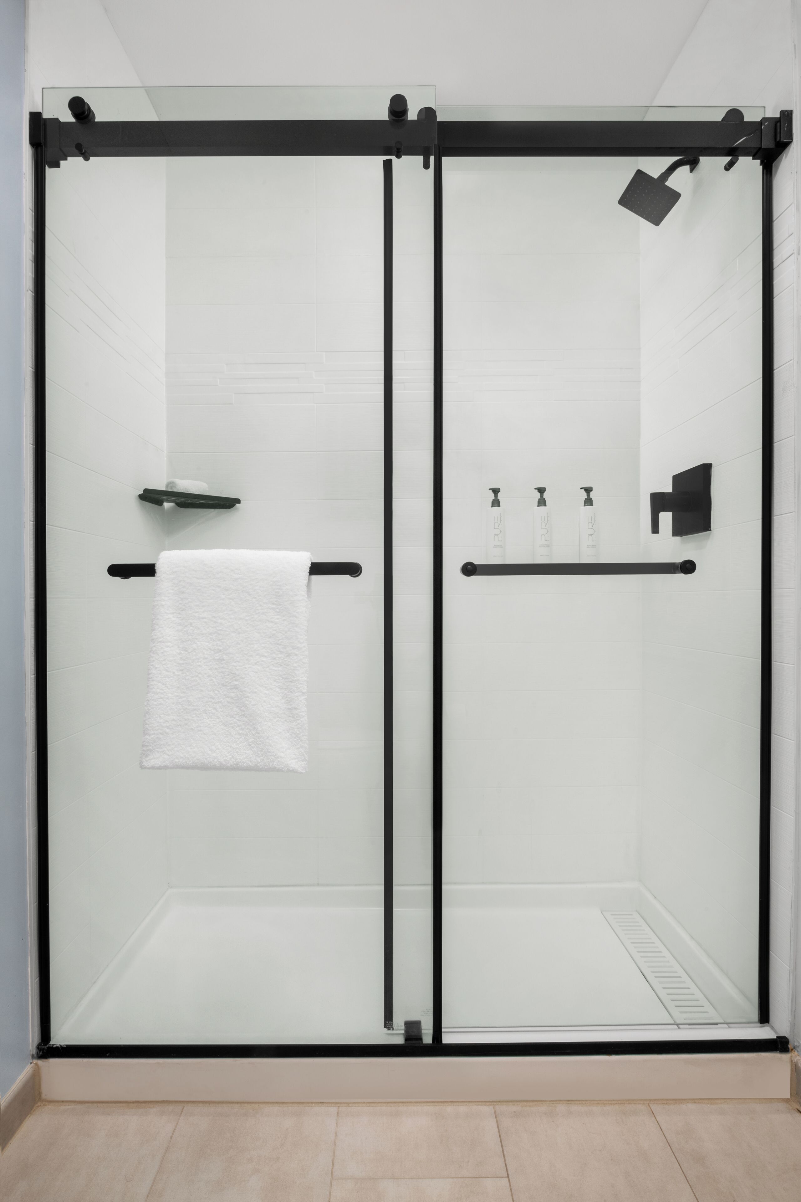 Een moderne badkamer met een douche met glazen wand, een handdoekhouder en een plank met toiletartikelen.
