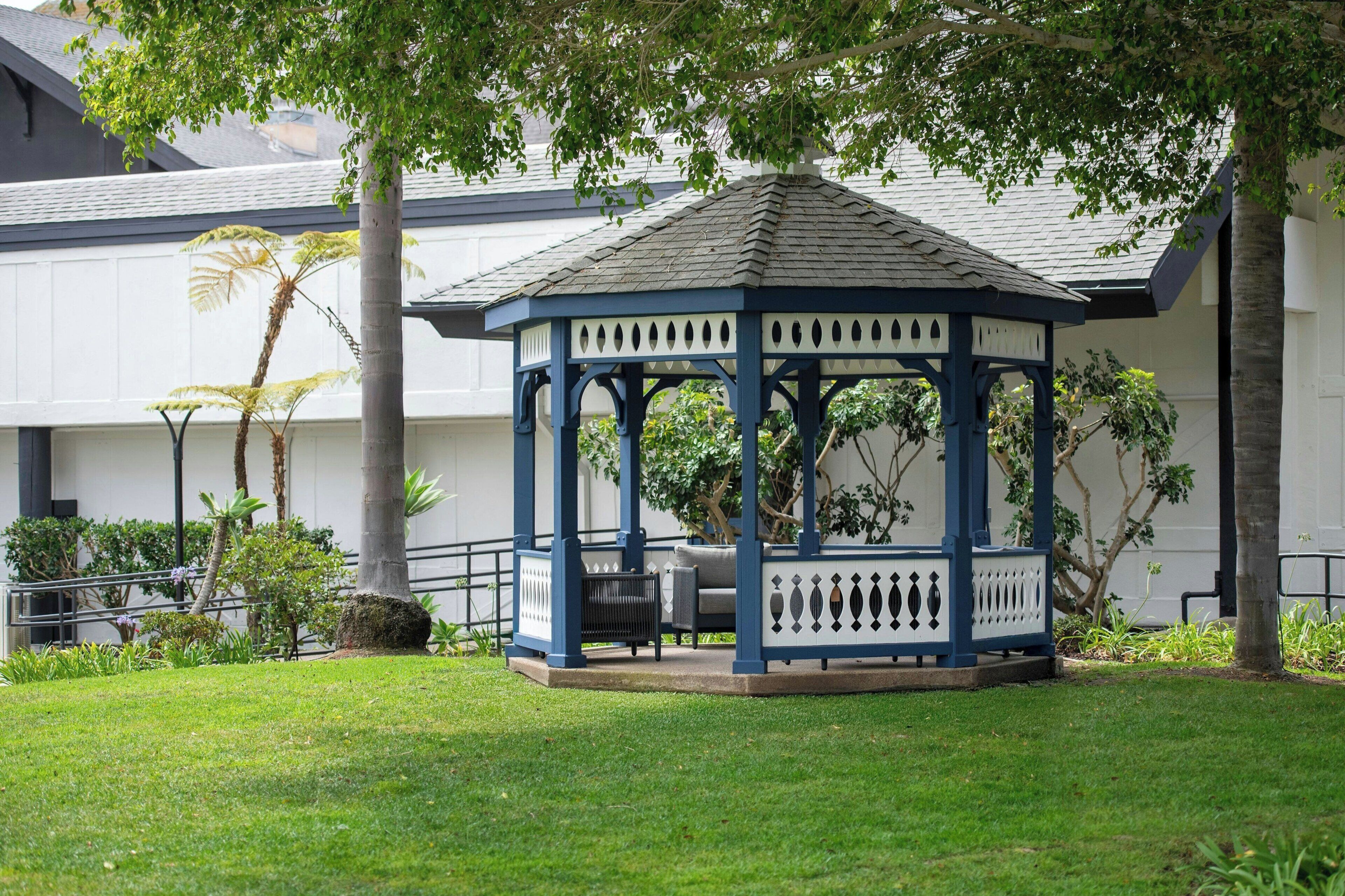 A gazebo with a blue and white color scheme, surrounded by a well-maintained lawn and various trees.