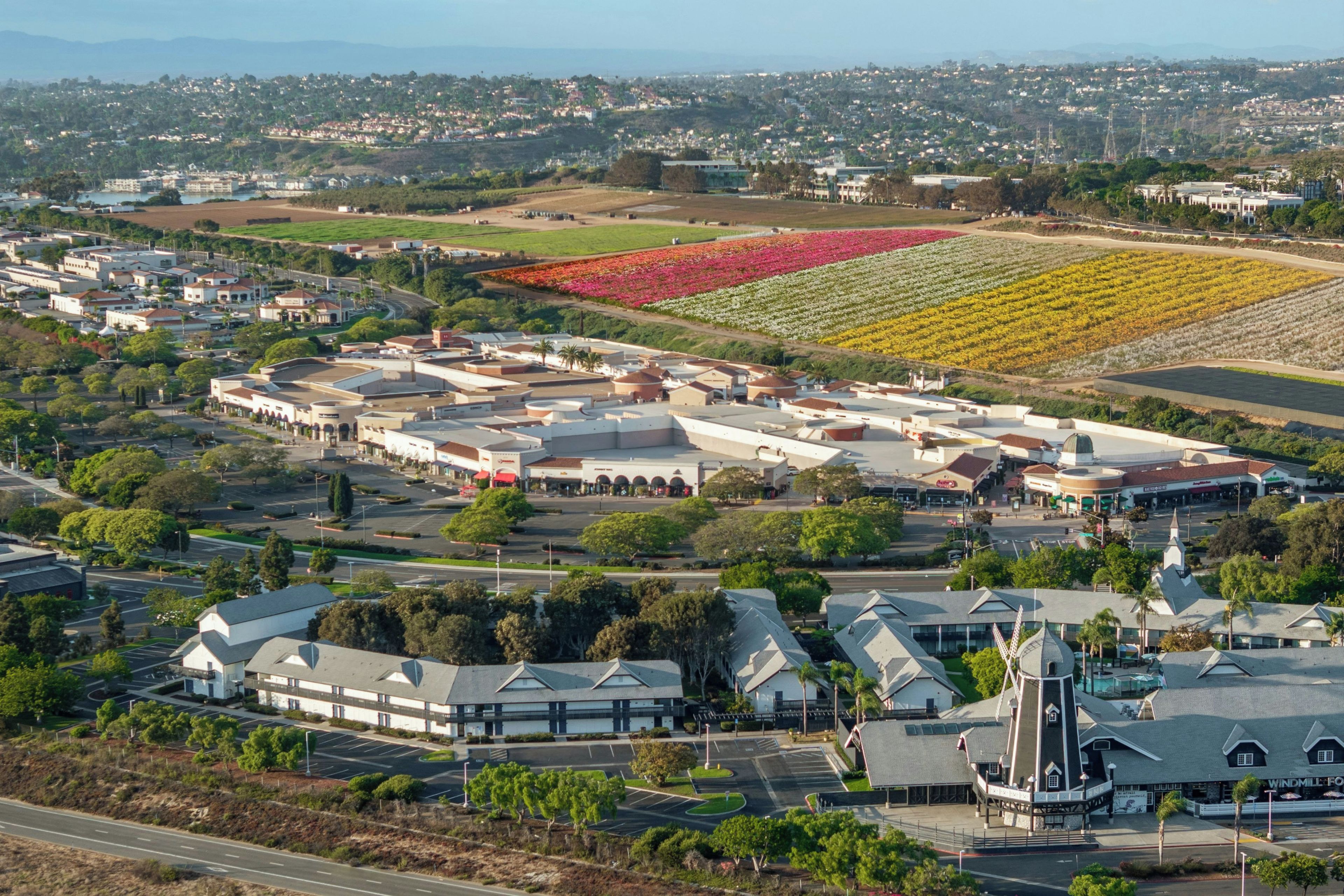 A large industrial complex with multiple buildings, parking areas, and a landscaped area with colorful flower beds.