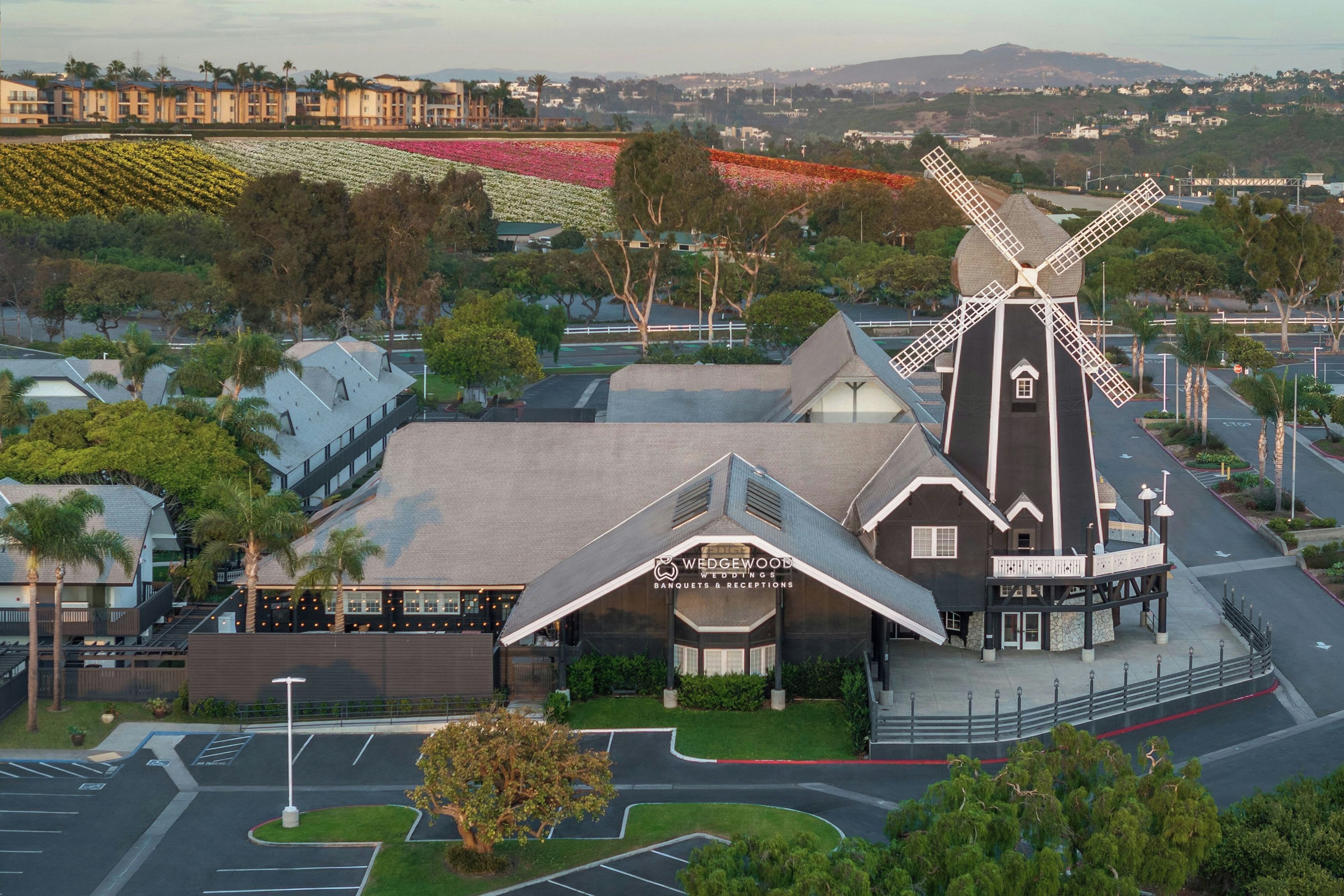 A building with a windmill, a parking lot, and a view of a flower field.