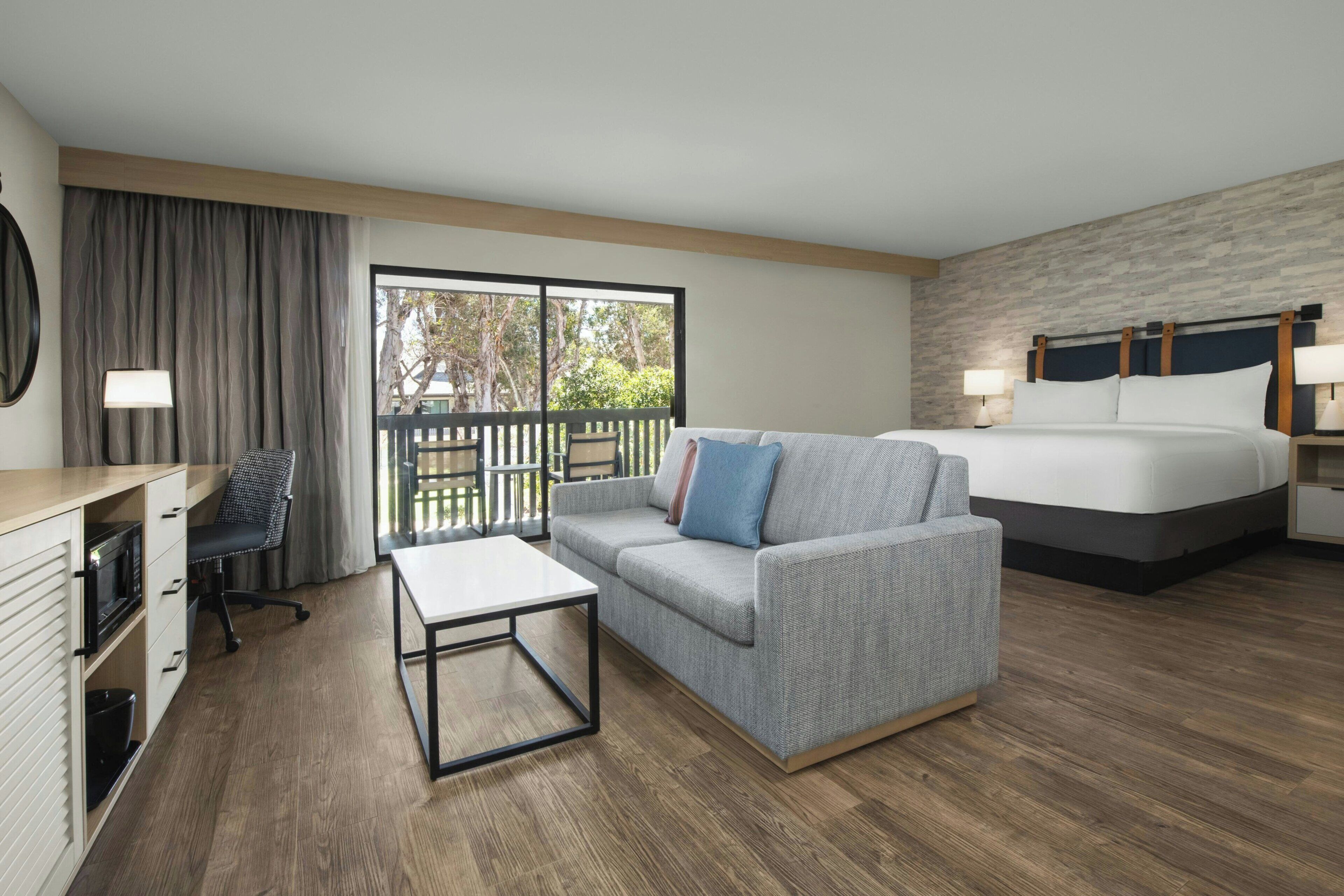 A hotel room with a bed, a sofa, a desk, and a balcony.