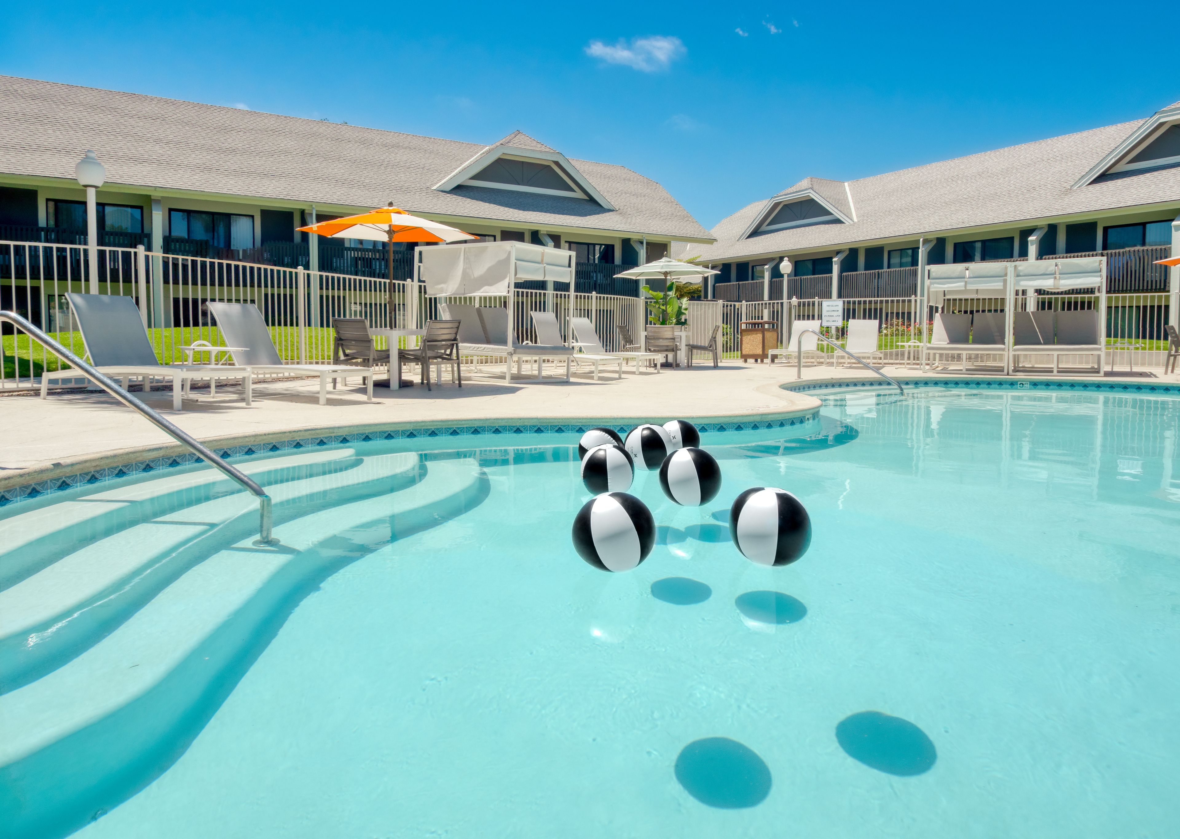 A swimming pool with lounge chairs and umbrellas, surrounded by a building with a tiled roof.