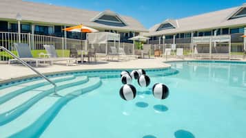 A swimming pool with lounge chairs and umbrellas, surrounded by a building with a tiled roof.