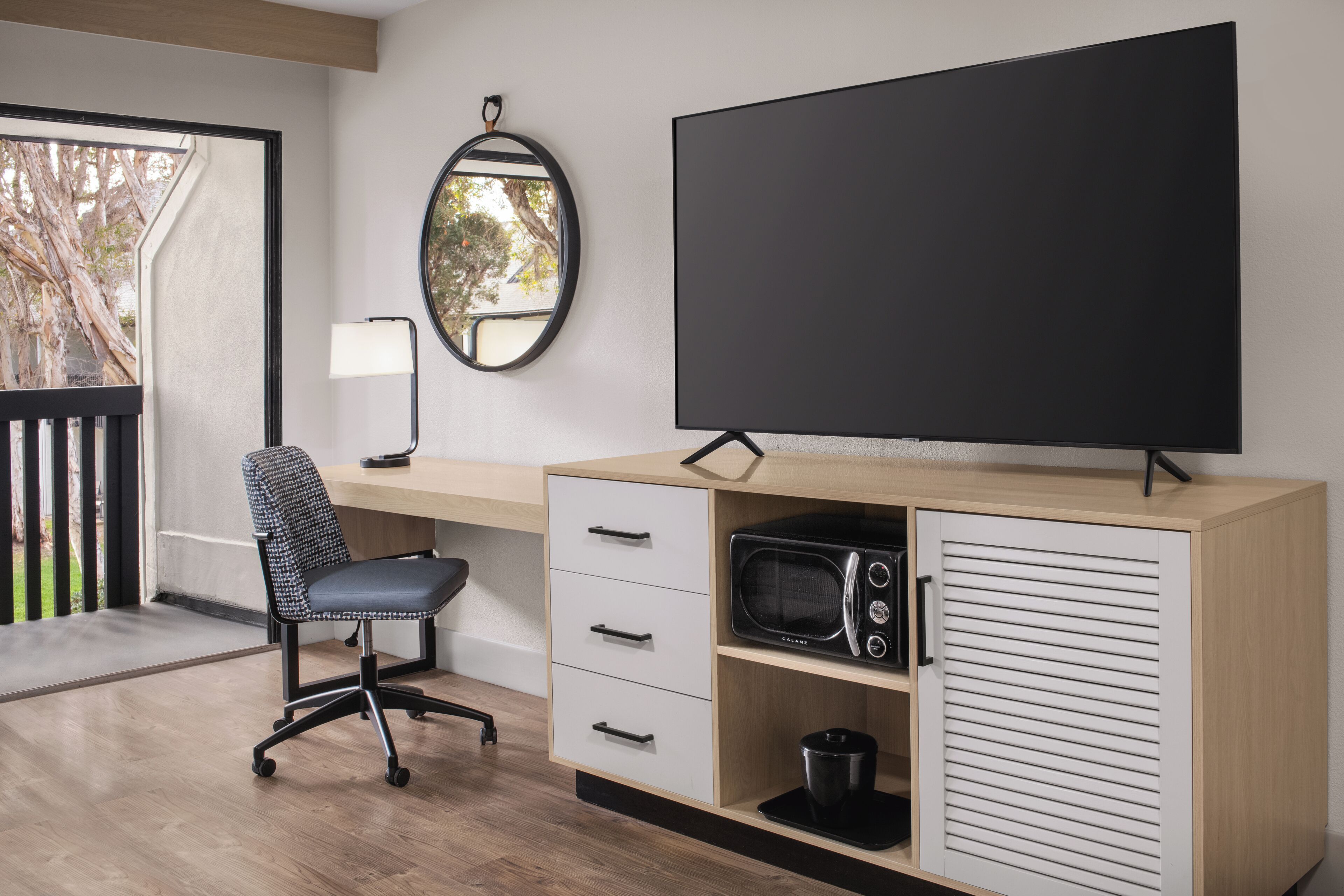 A modern office space with a desk, chair, television, and a small cabinet with a microwave.