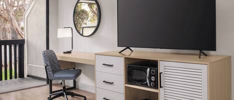 A modern office space with a desk, chair, television, and a small cabinet with a microwave.