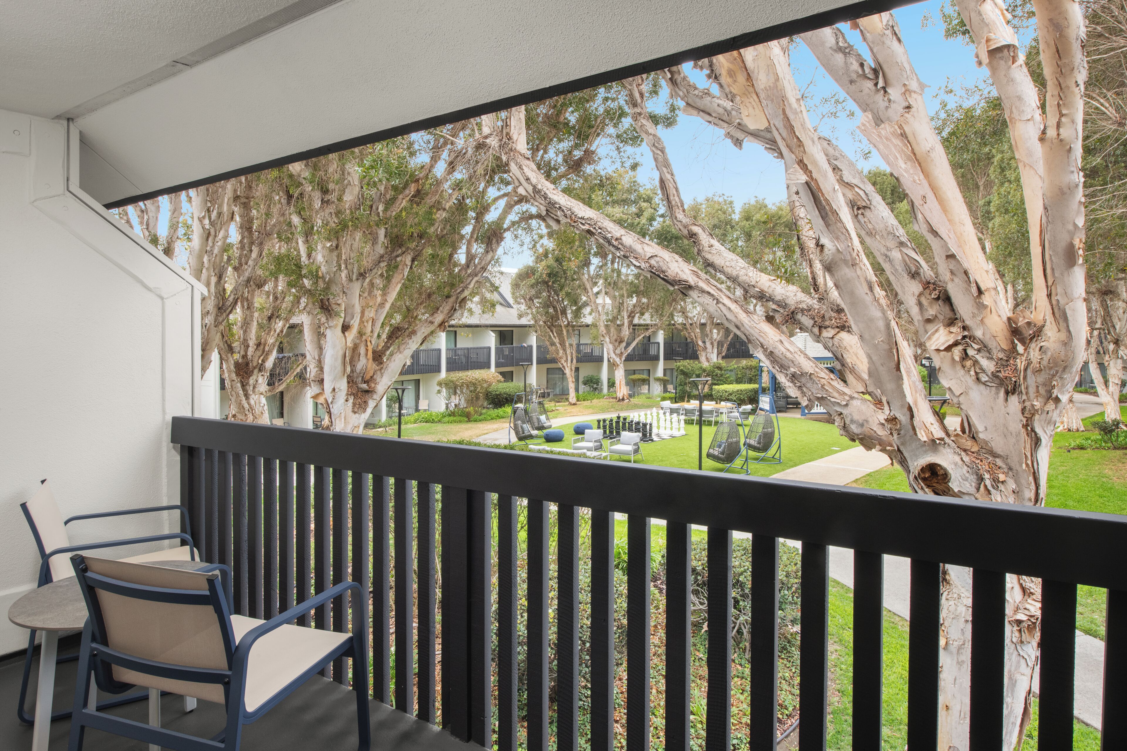 A balcony with a view of a courtyard, featuring a chessboard and outdoor furniture.