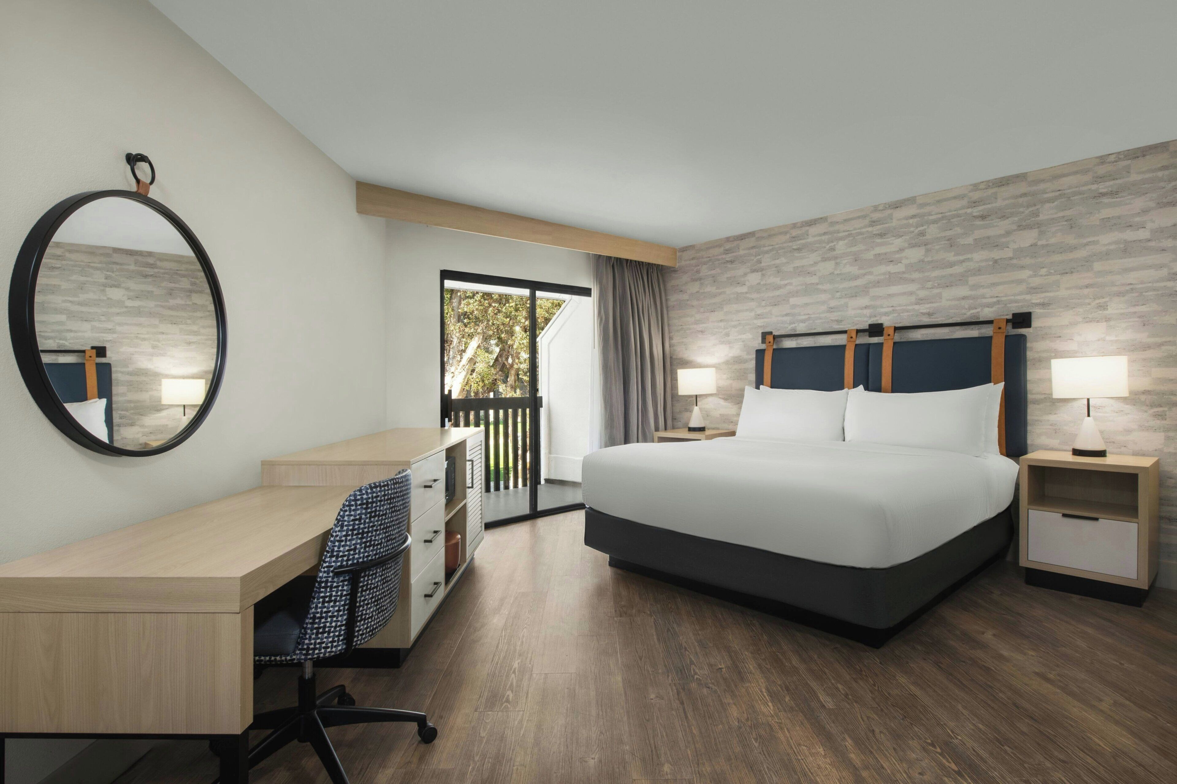 A hotel room with a bed, desk, chair, and a large mirror.