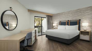 A hotel room with a bed, desk, chair, and a large mirror.