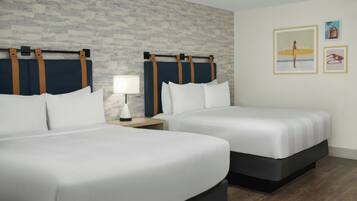 A hotel room with two beds, a nightstand, a lamp, and a brick-patterned wall.