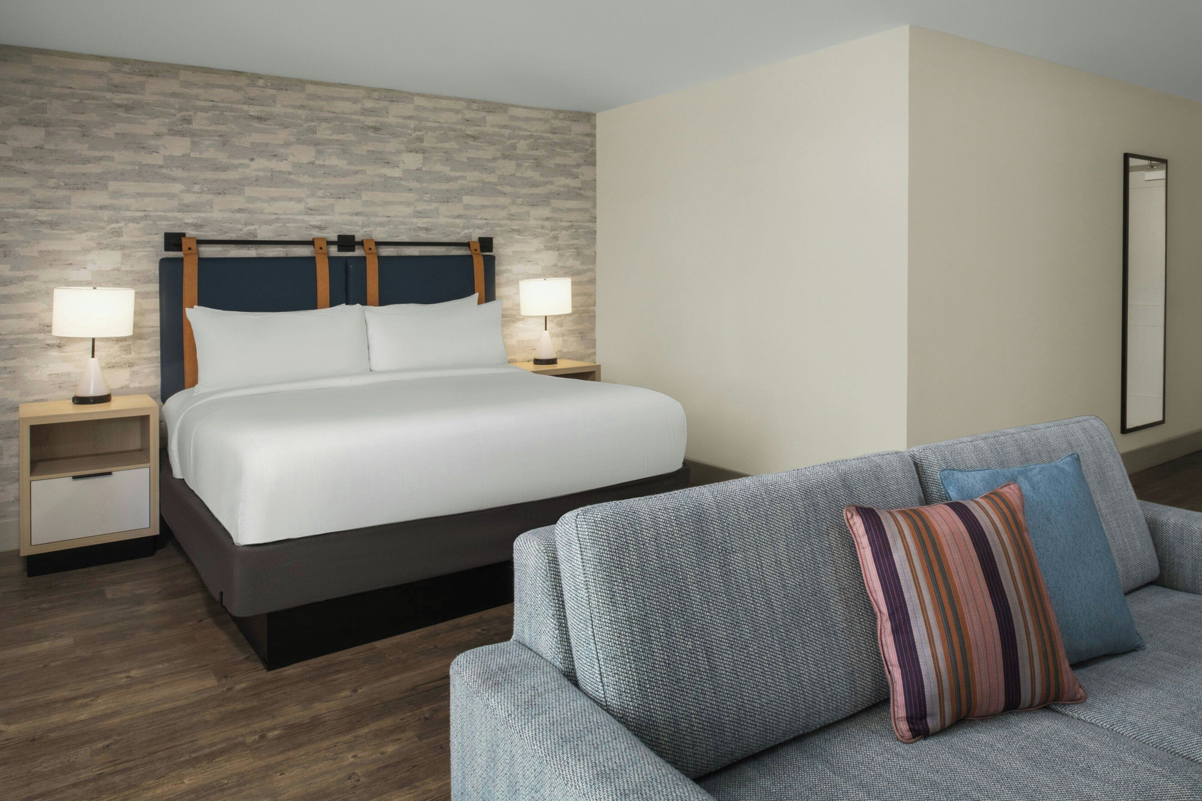 Une chambre d’hôtel comprenant un lit, deux tables de chevet avec des lampes, un canapé et un miroir fixé au mur.