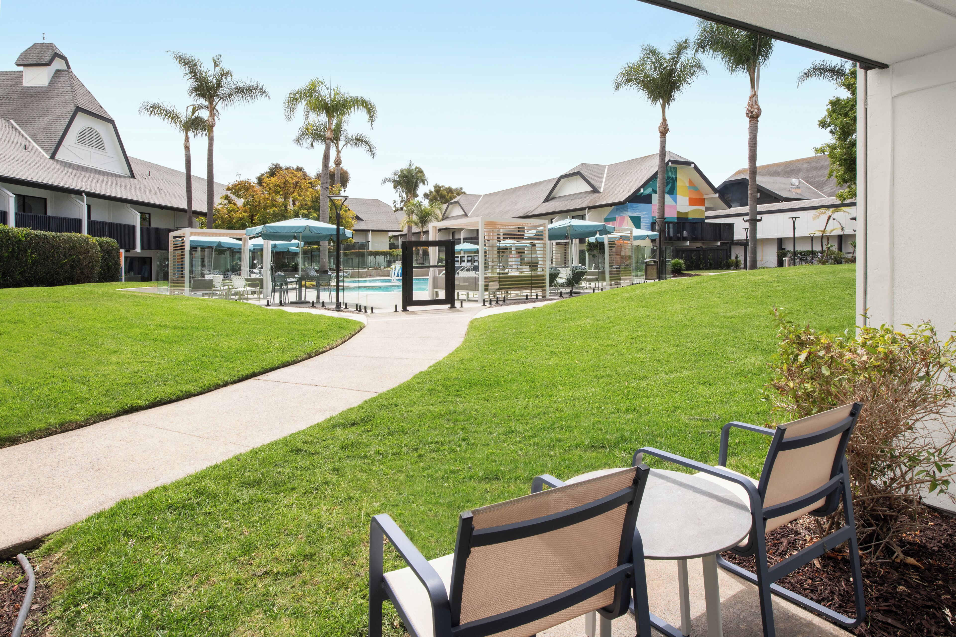 Une cour avec une piscine, des espaces de détente en plein air et des palmiers.