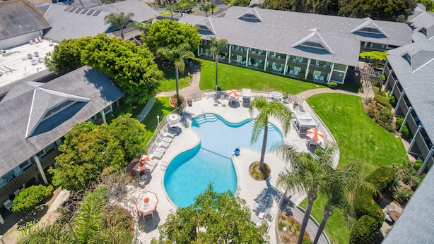 An aerial view of a resort with a swimming pool, palm trees, and a view of the ocean.
