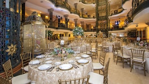 Un gran salón de baile con candelabros ornamentados, balcones escalonados y mesas elegantemente dispuestas.
