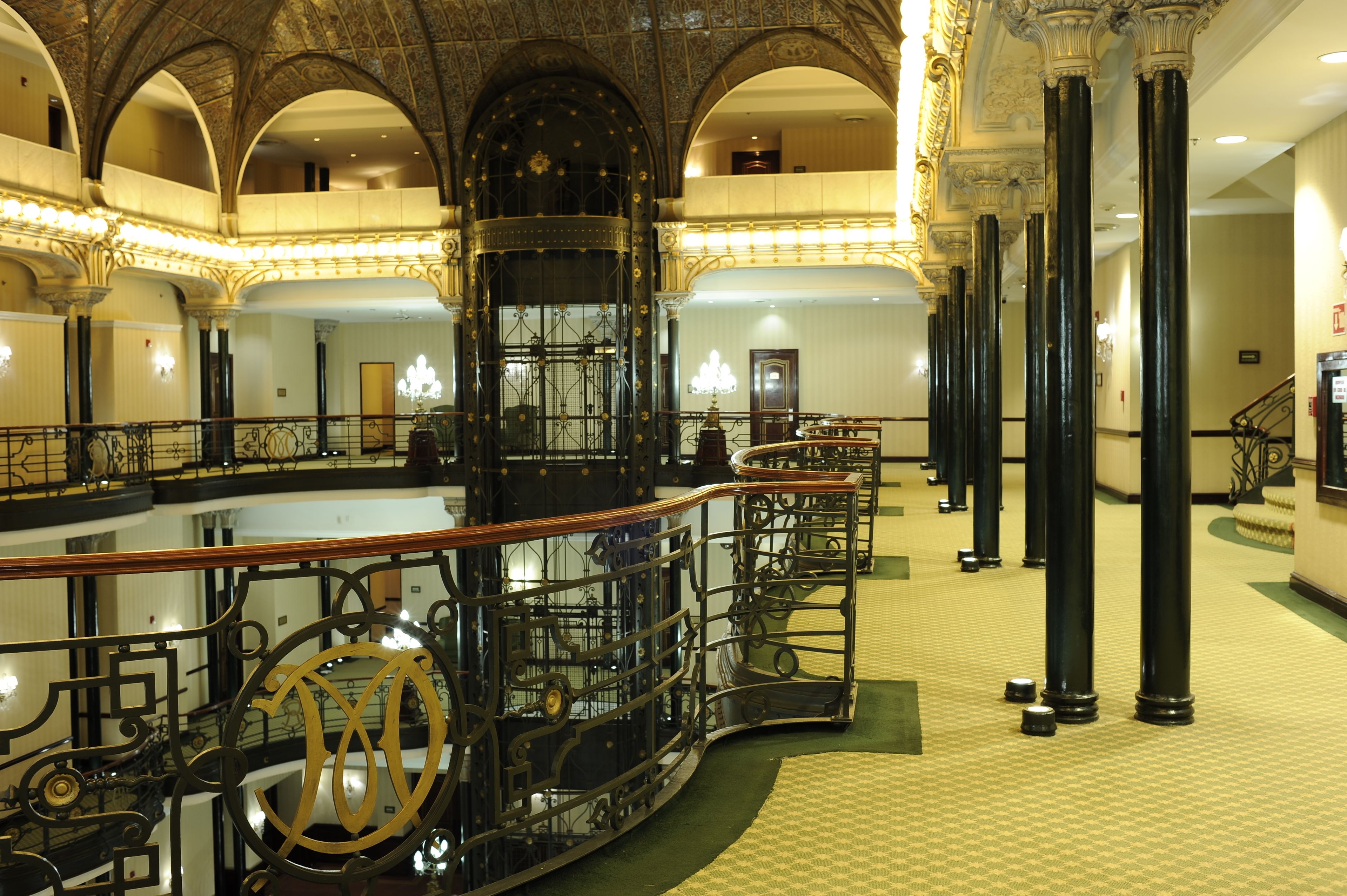 A grand lobby with ornate columns, a central staircase, and a chandelier.