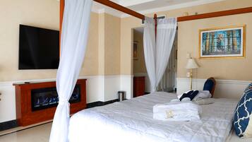 A hotel room with a large bed, a flat-screen TV mounted on the wall, a fireplace, and a painting on the wall.