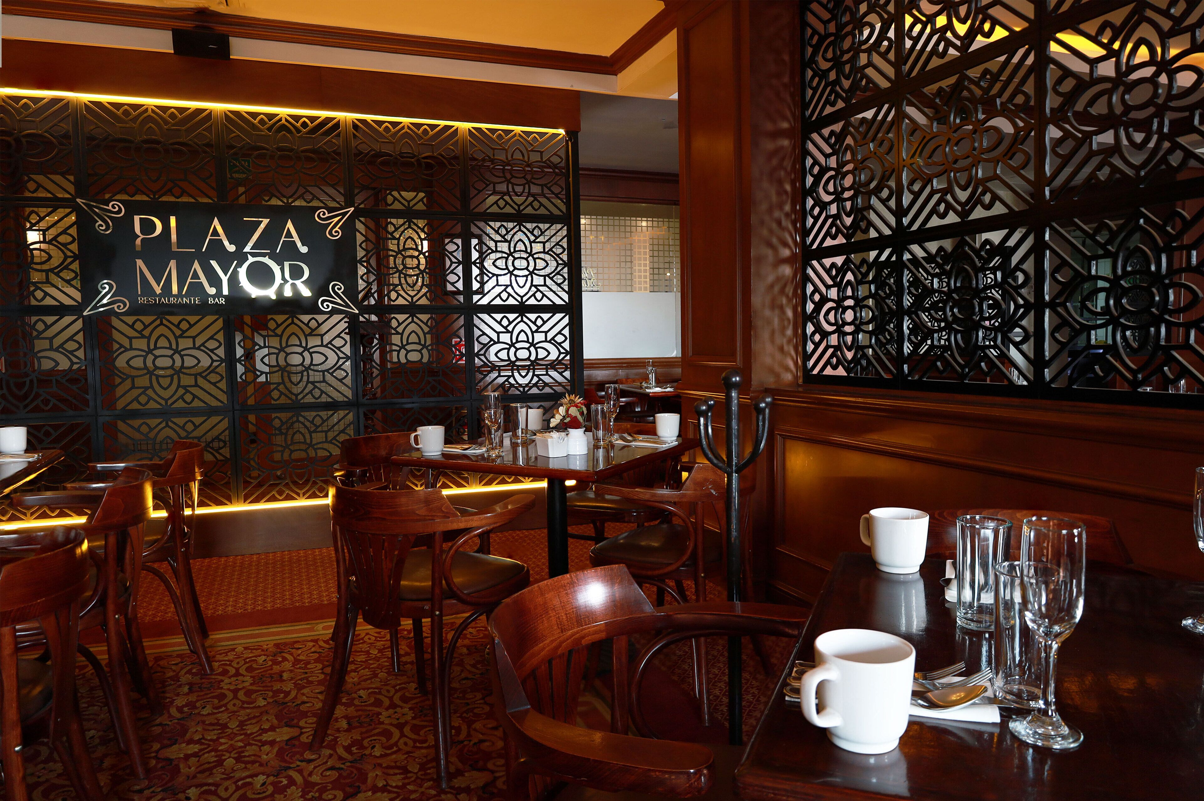 Interior de restaurante con mobiliario de madera, pared con estampado y un cartel que dice "PLAZA MAYOR".