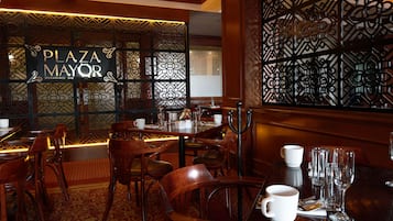 Interior de restaurante con mobiliario de madera, pared con estampado y un cartel que dice "PLAZA MAYOR".