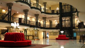 Un vestíbulo espacioso con una imponente escalera, asientos rojos y candelabros ornamentales.