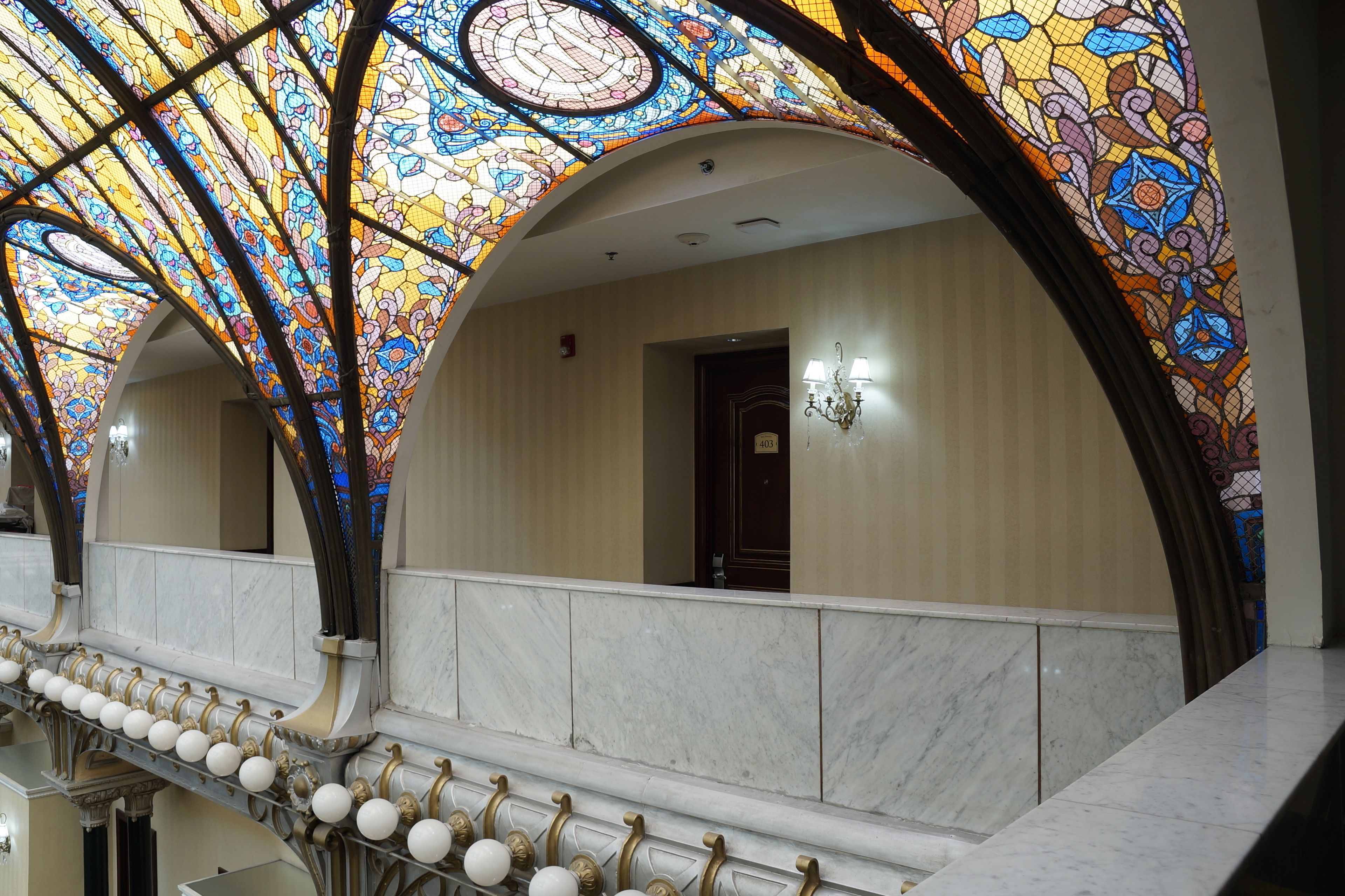 A grand hall with ornate stained glass ceiling, marble walls, and a series of white spherical decorations along the lower edge.