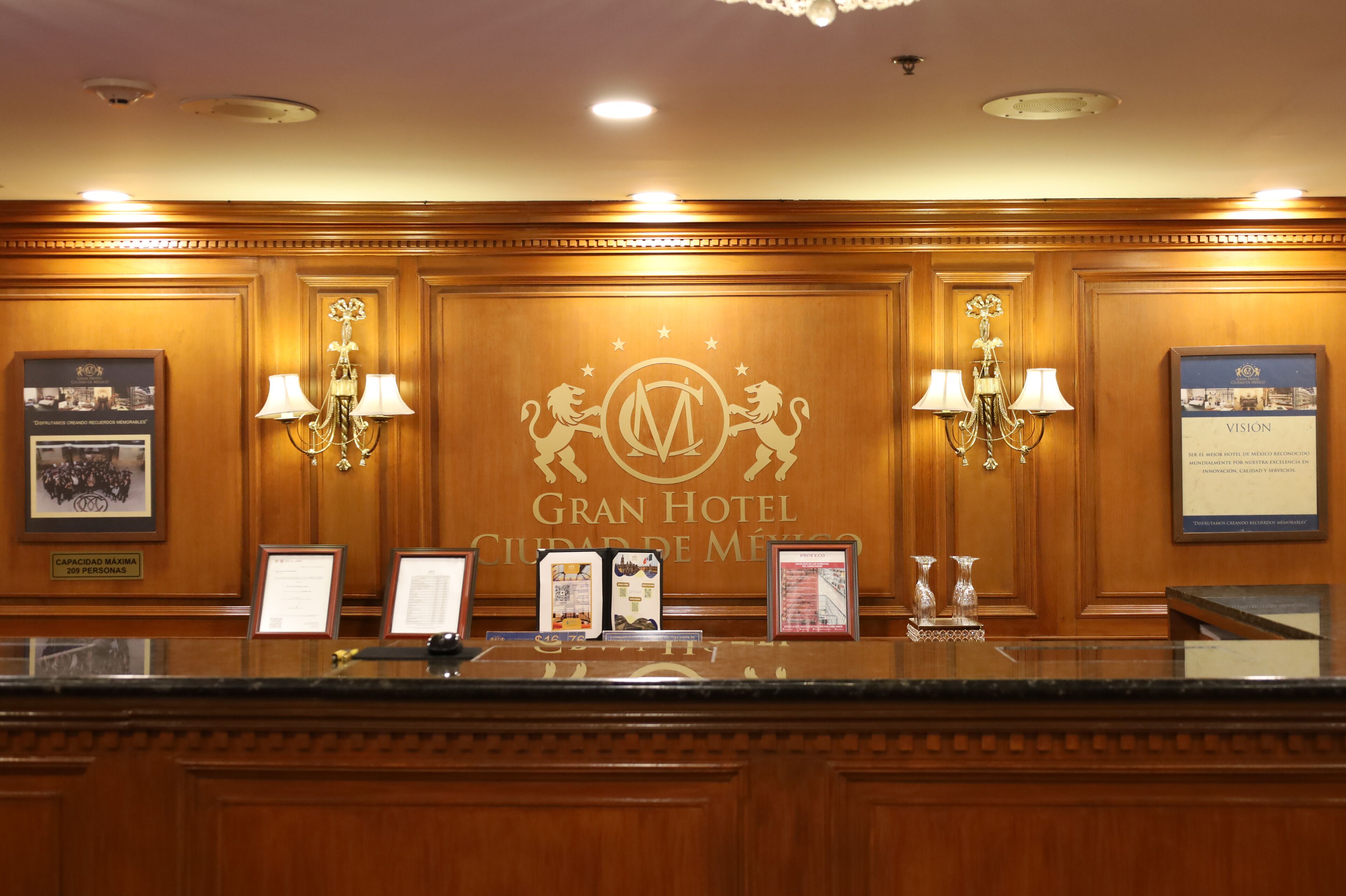 Un comptoir d’accueil dans le Gran Hotel Ciudad de México, agrémenté d’un logo, de tableaux encadrés et d’un lustre.