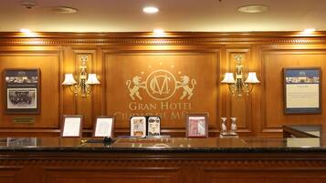 Un comptoir d’accueil dans le Gran Hotel Ciudad de México, agrémenté d’un logo, de tableaux encadrés et d’un lustre.