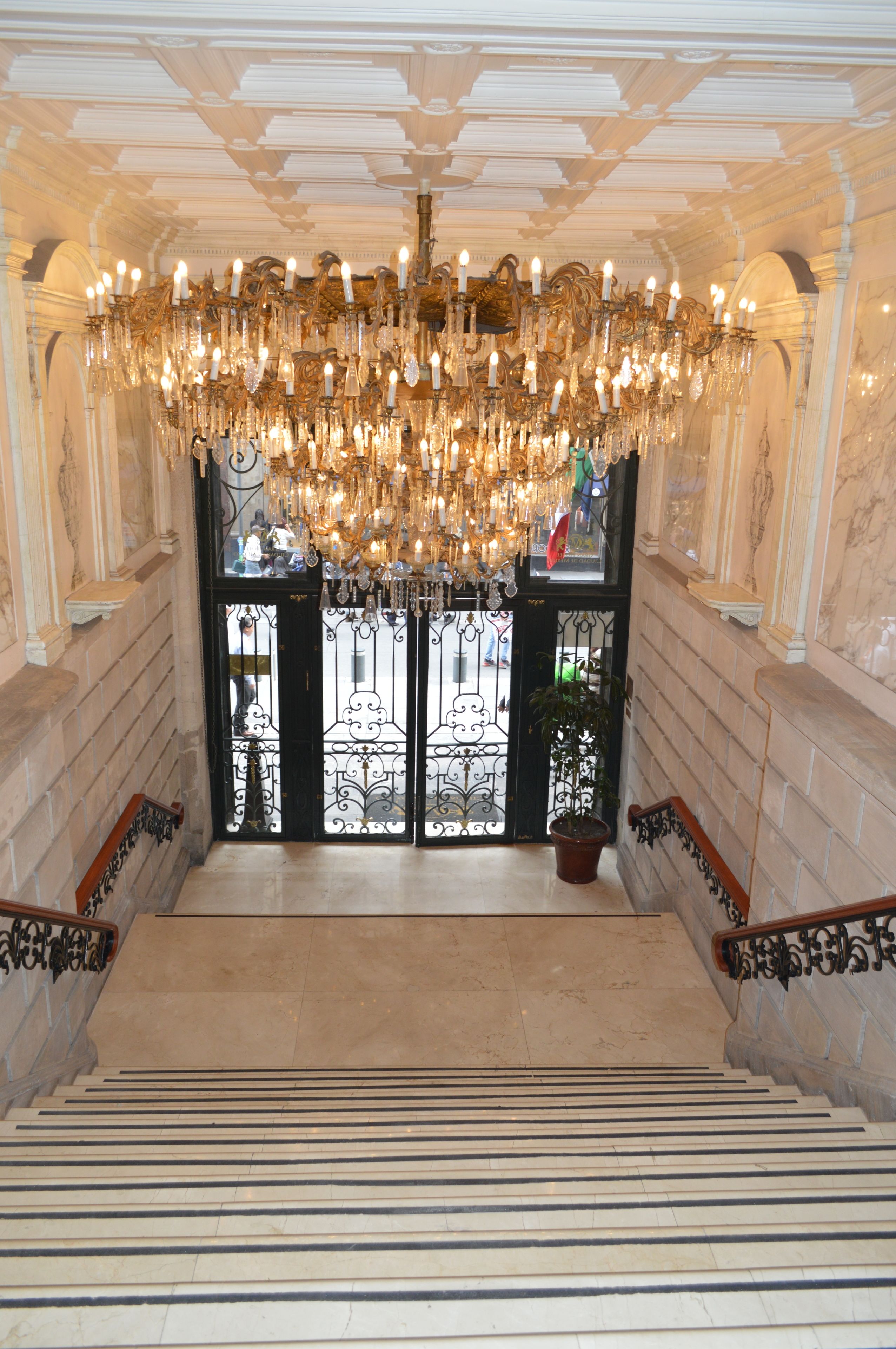 Una majestuosa escalera conduce a un salón con una gran lámpara de araña ornamentada.