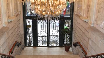 Una majestuosa escalera conduce a un salón con una gran lámpara de araña ornamentada.