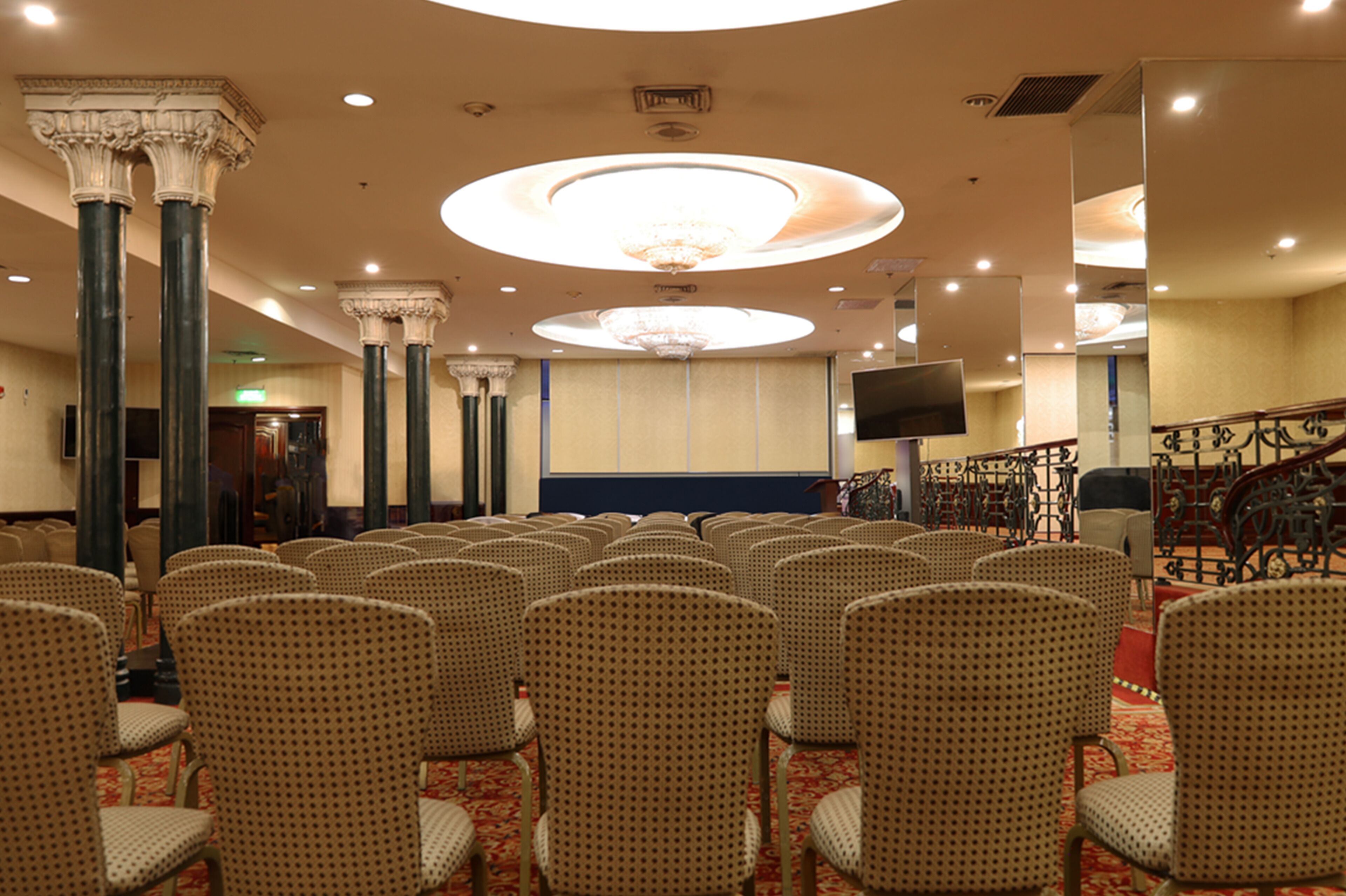 Un salón de conferencias con filas de sillas, una lámpara de araña grande y una pantalla de televisión.
