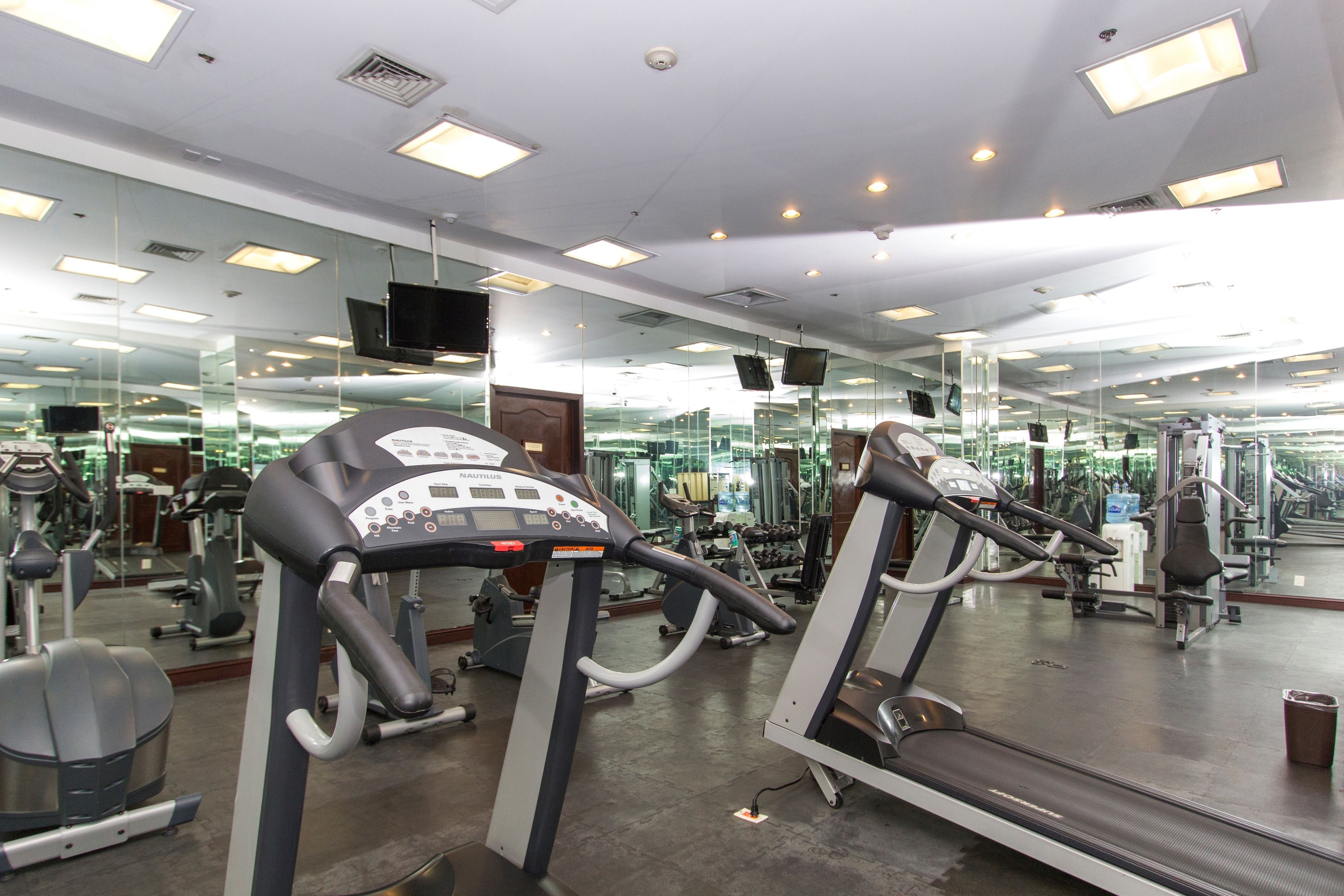 Un gimnasio con cintas de correr, máquinas de pesas y un espejo grande.