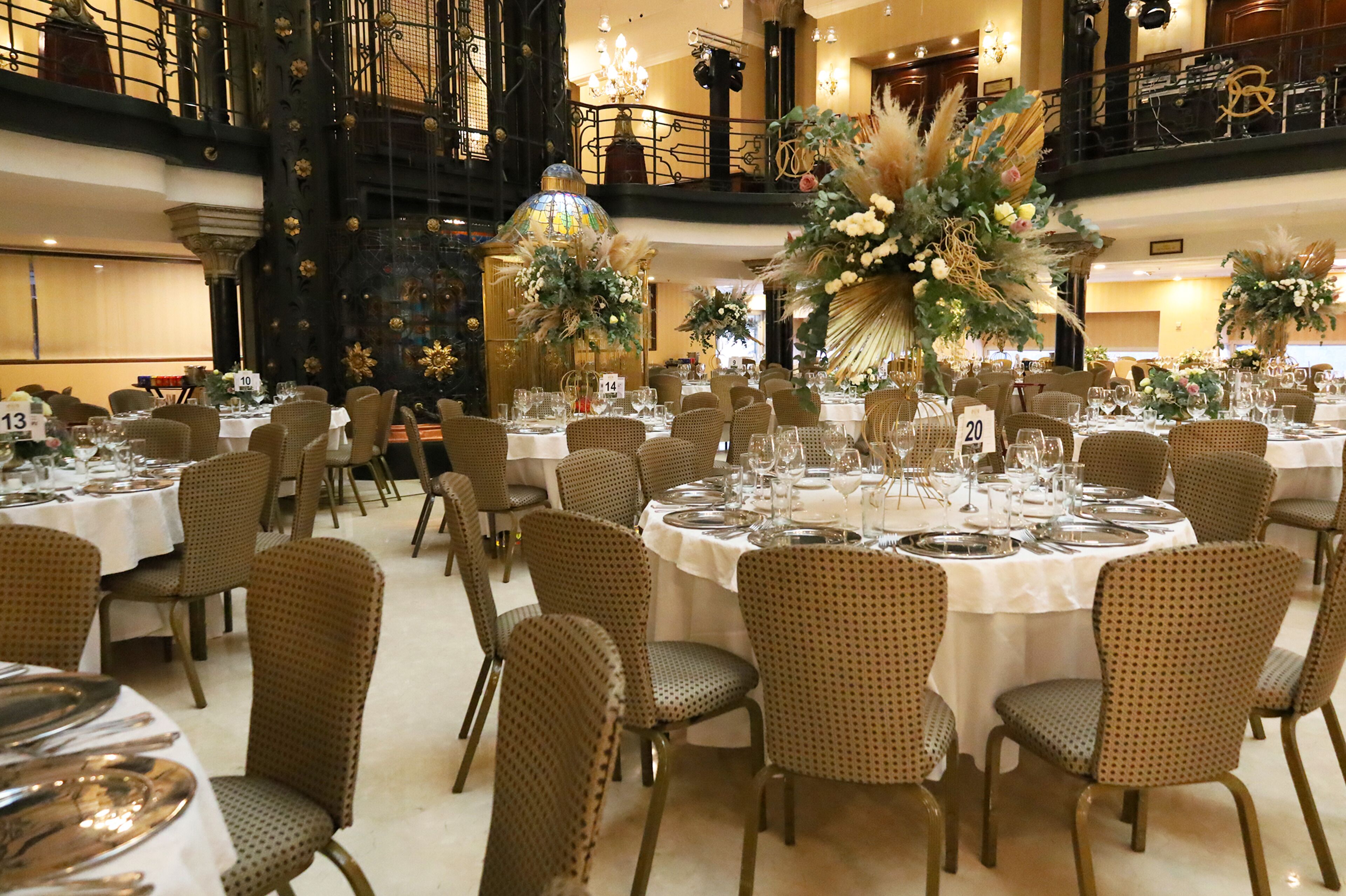 Ein Festsaal mit runden Tischen, Korbstühlen und floralen Tischdekorationen.