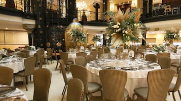 Ein Festsaal mit runden Tischen, Korbstühlen und floralen Tischdekorationen.