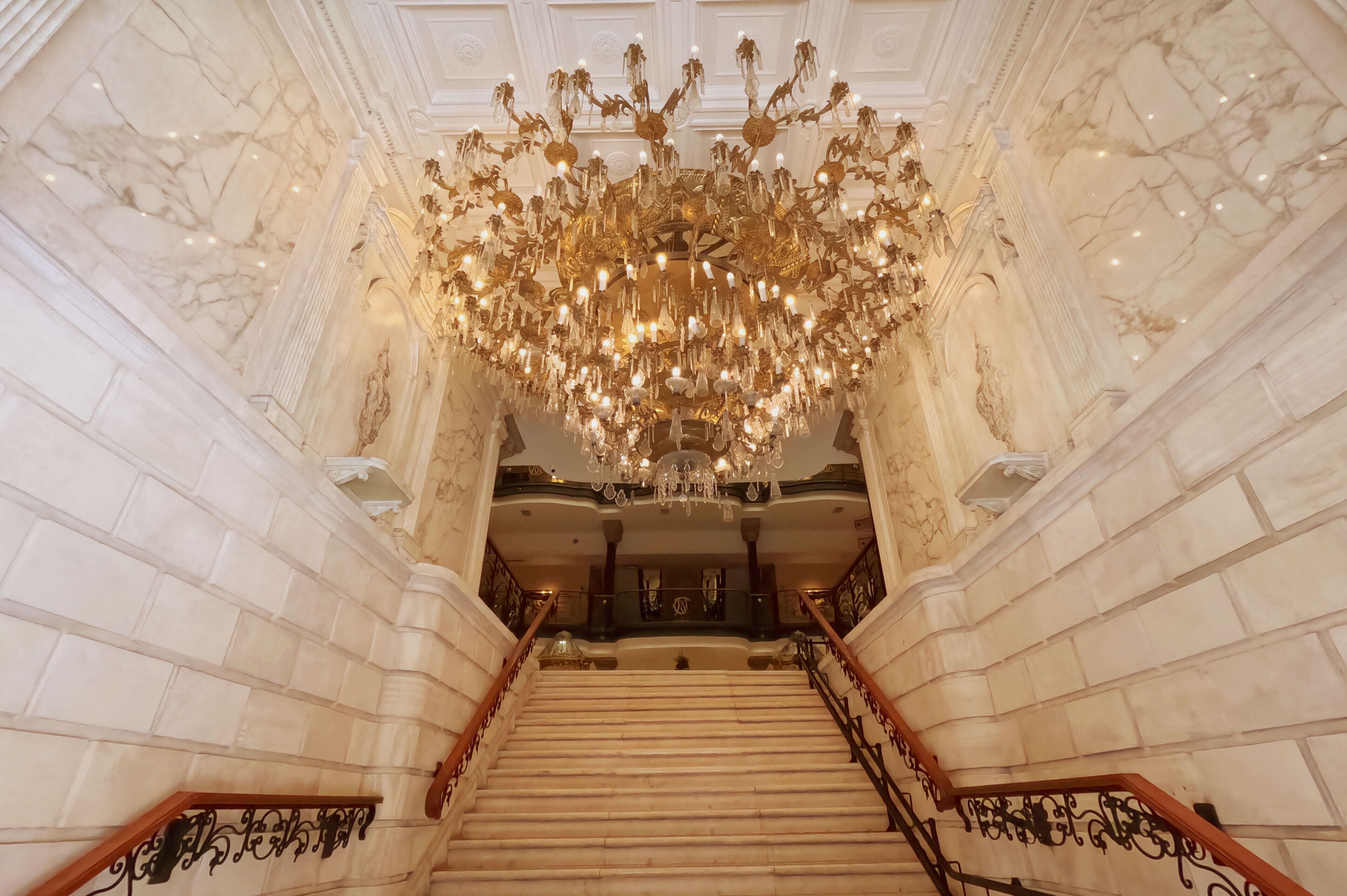 Una gran escalera con una lámpara de araña grande, paredes de mármol y barandillas ornamentadas.