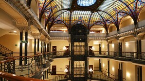 Un atrio de varios niveles con ornamentales barandillas de hierro, una escalera central y un techo de vitrales.
