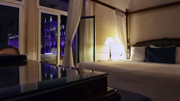 A hotel room with a bed, a nightstand, a lamp, and a view of a lit-up building outside.