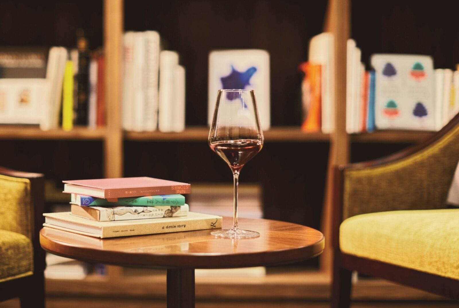 Un bicchiere di vino su un tavolino rotondo, con una pila di libri sullo sfondo.