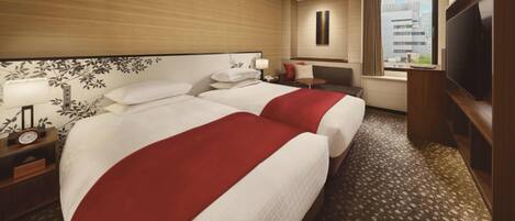 A hotel room with two beds, a TV, a desk, and a window with a city view.