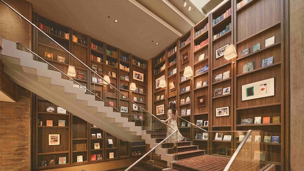 A modern library with a central staircase surrounded by bookshelves, a glass railing, and a unique metal sculpture at the bottom. - Shiba Park Hotel (Tokyo)