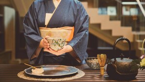 A person in traditional attire holding a teapot and a cup, with a table set for tea. - Shiba Park Hotel (Tokyo)