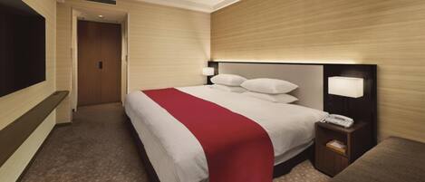 A hotel room with a large bed, a bedside table with a lamp, a TV mounted on the wall, and a door leading to another room.