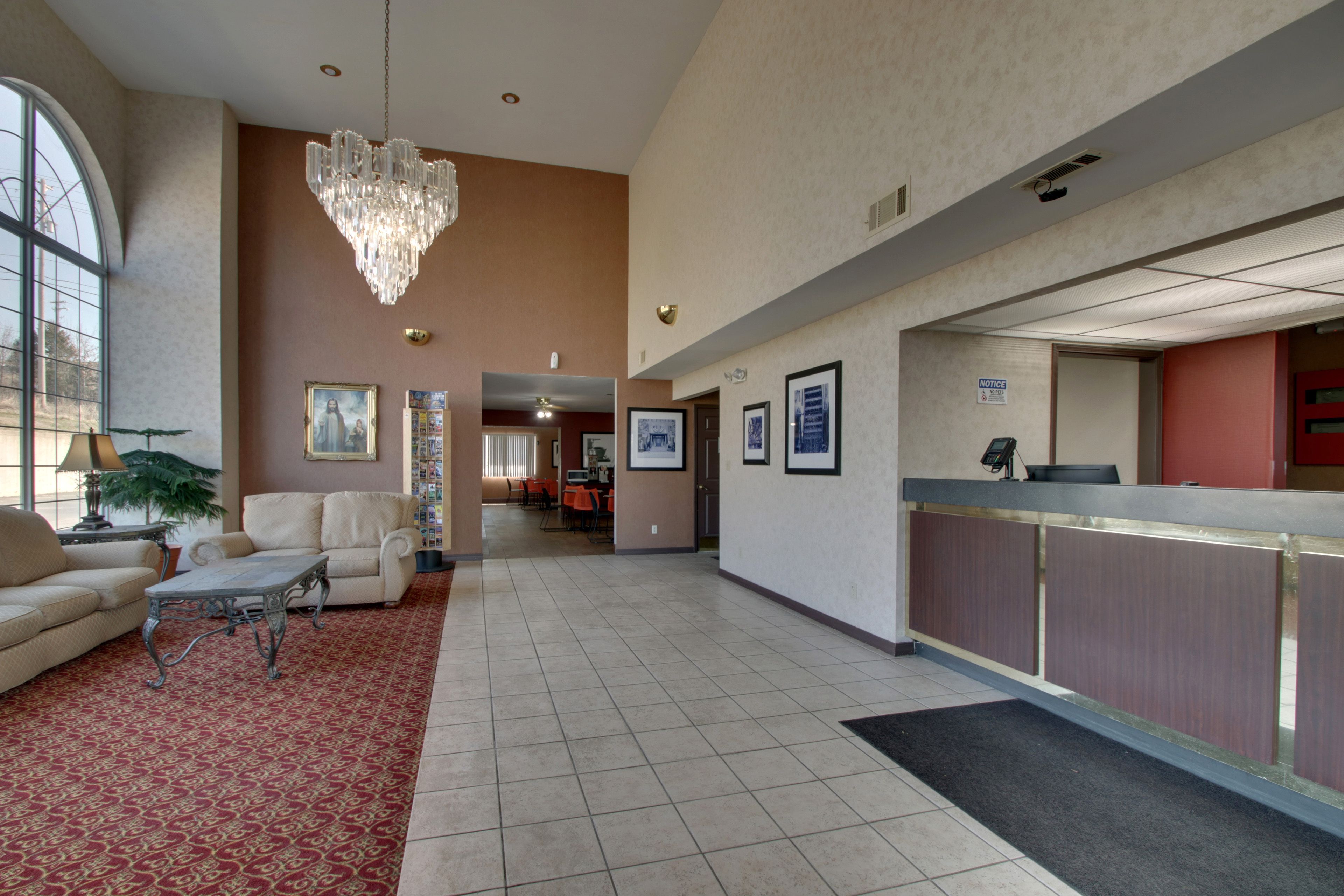 A spacious lobby with a reception desk, a chandelier, a red carpet, and a large window.