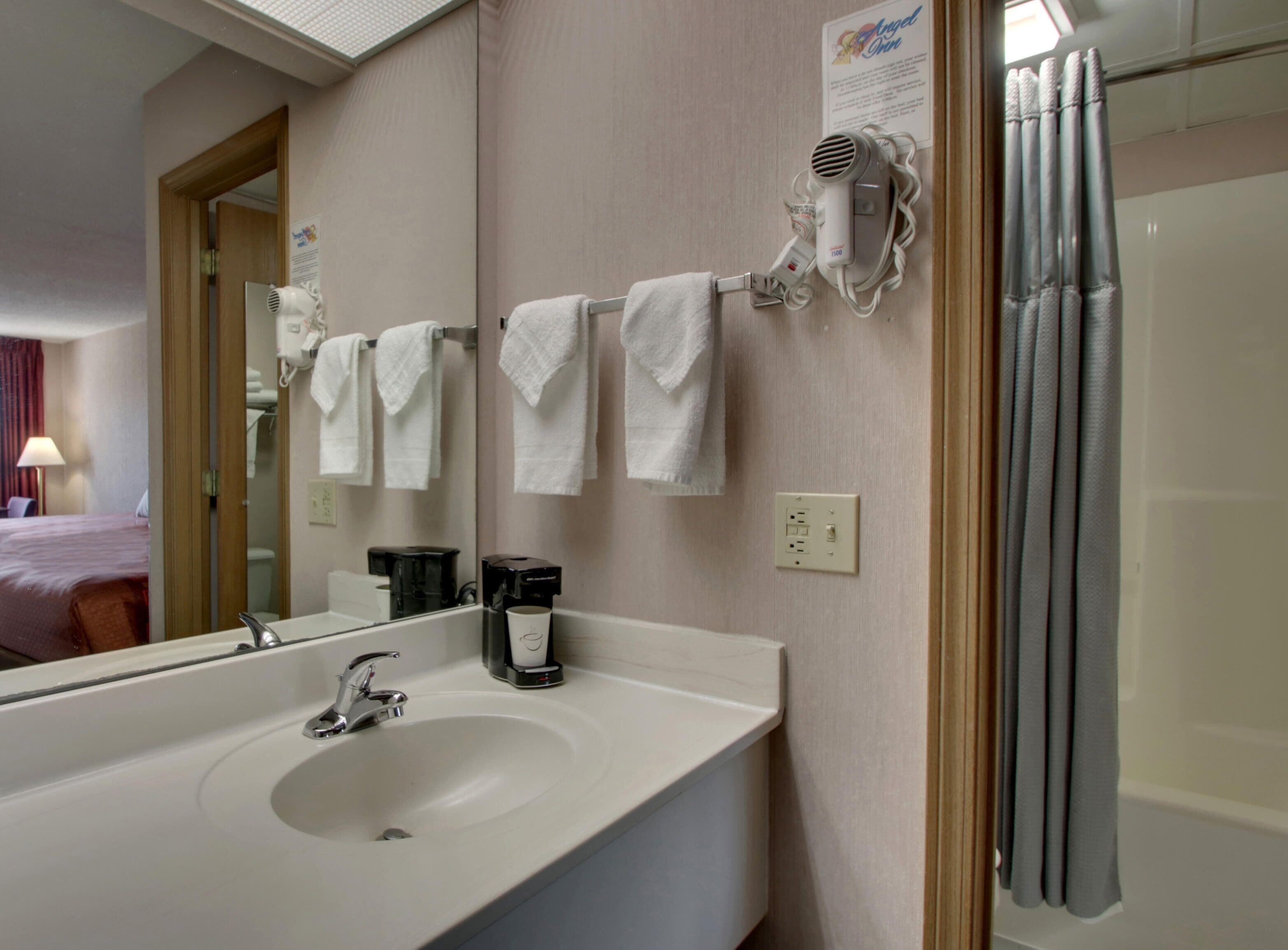 A hotel bathroom with a sink, a hairdryer, a mirror, and a shower curtain.