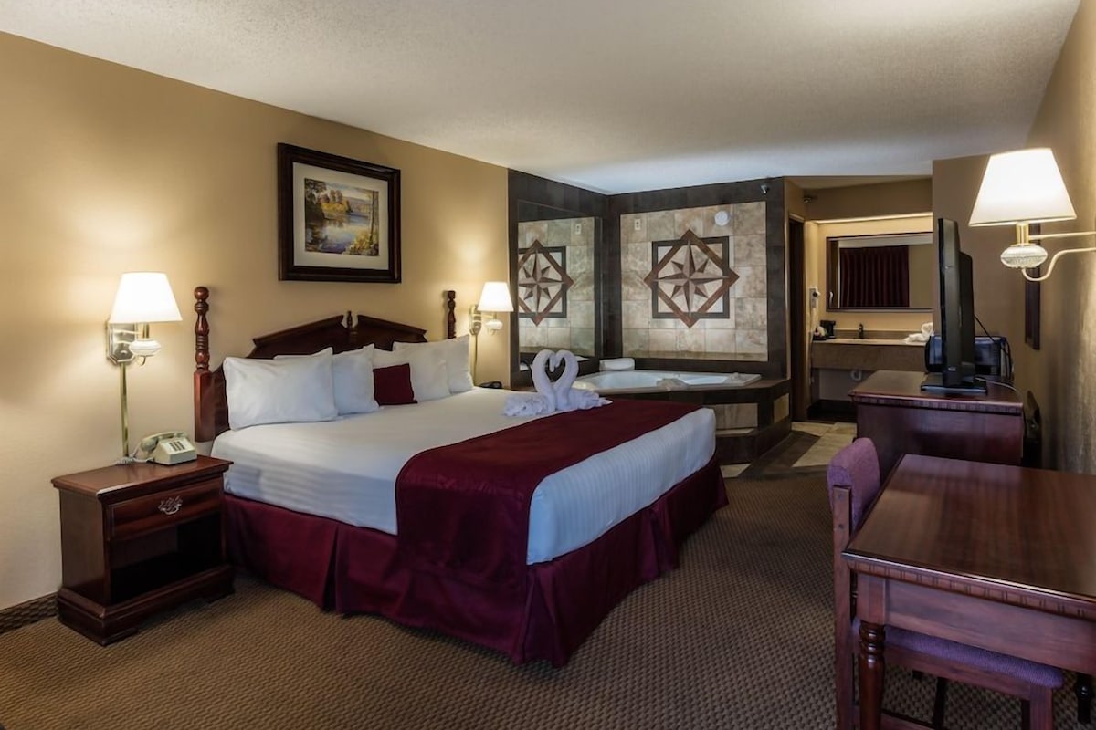 A hotel room with a large bed, two bedside tables, a desk, and a bathroom with a bathtub.