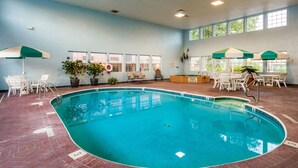 An indoor swimming pool with clear blue water, surrounded by white lounge chairs and tables, and large windows allowing natural light. - Angel Inn Central (Branson)