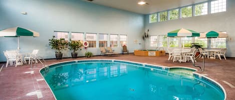 An indoor swimming pool with clear blue water, surrounded by white lounge chairs and tables, and large windows allowing natural light.
