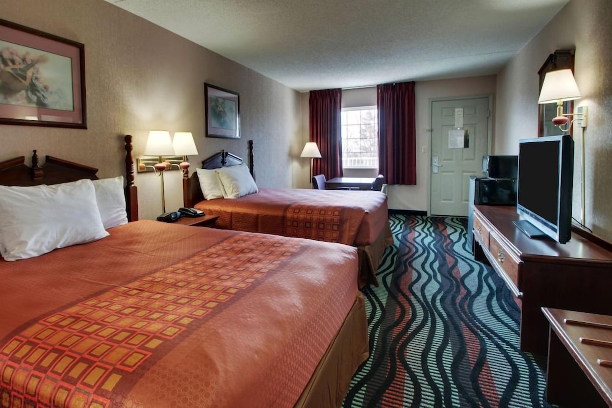 A hotel room with two beds, a desk, a television, and a patterned carpet.